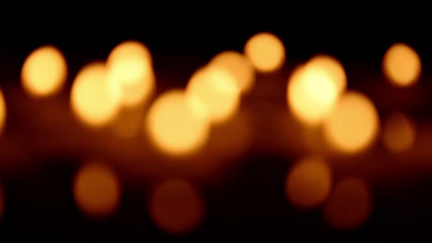 Defocused candle bokeh forms shifting warm orbs as light intensity changes , creating smooth motion in the blurred golden patterns of distant flames.