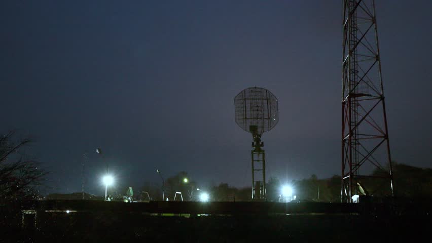 Large military radar stands illuminated against dark sky, scanning Russian country borders. Bright floodlights highlight defense infrastructure in remote environment