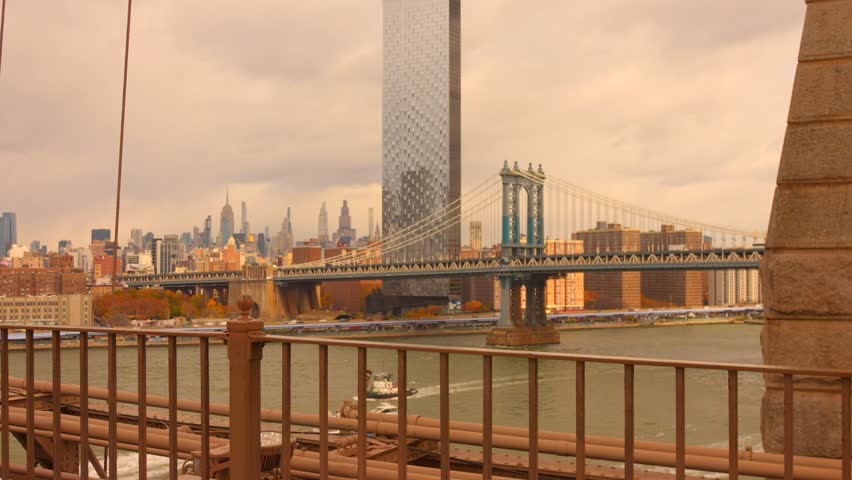 The pedestrian walkway of the Brooklyn Bridge, looking across the East River to the Manhattan Bridge and the Lower Manhattan skyline, featuring modern towers and river.