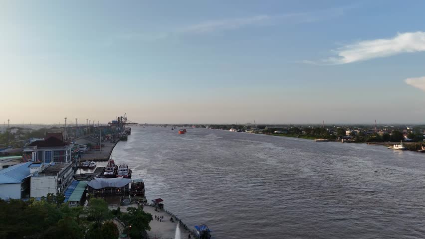 A wide Kapuas River flows through the bustling port city, with docks, ships, and riverside roads.