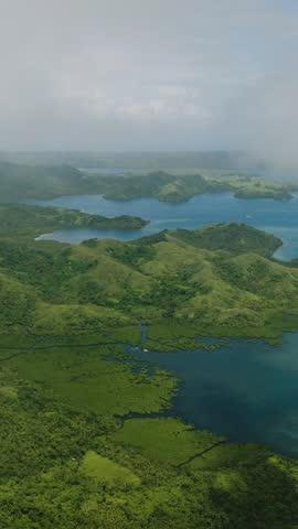 Aerial view of green hills with lagoons and blue sea extending to horizon under clouds. Siargao, Philippines.