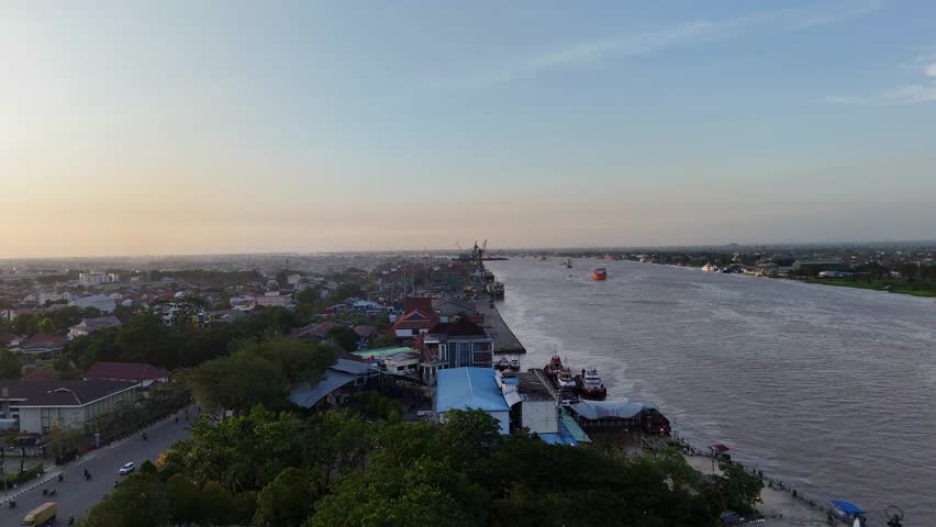 Beautiful afternoon drone flight over Pontianak, Indonesia. Showcasing the huge Kapuas River, city buildings, and port activity under warm evening light.