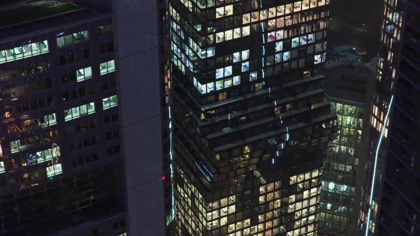 Aerial top down view of modern skyscrapers in Frankfurt financial district at night. Illuminated windows reveal offices with workers inside