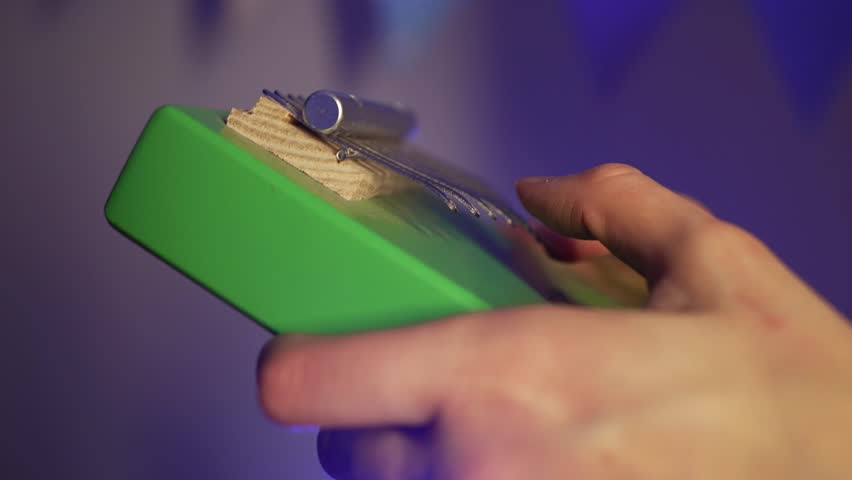 Musician plucking delicate tines of green kalimba, creating soothing melodic sounds with graceful finger movements during intimate musical performance