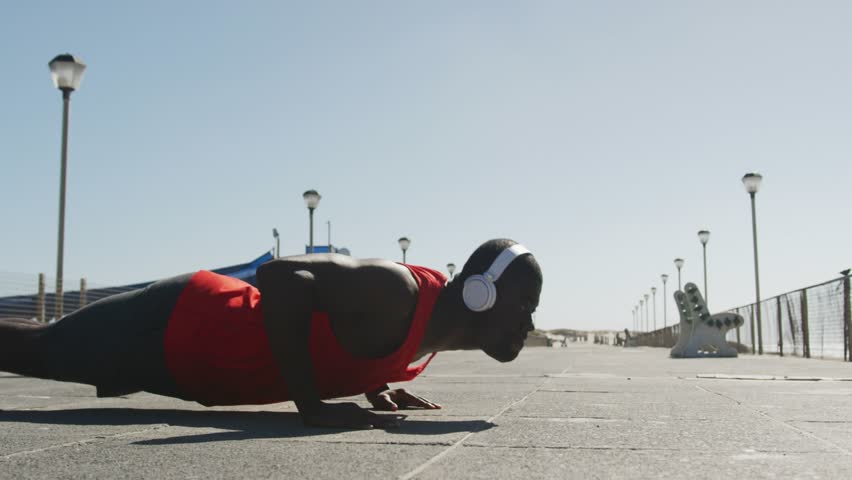 Man starting low and performing push-ups for fitness while GOOD VIBES title partly obscuring torso. Fitness, workout, calisthenics, seaside, promenade, headphones, reps