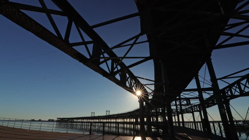 Dramatic low-angle view of Muelle del Rio Tinto structure, Huelva, Spain. Industrial heritage, engineering framework, and sun starburst.
