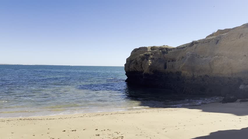 a gorgeous summer landscape at the beach with large rocks in silky brown sand surrounded by blue ocean water and waves rolling into the beach with powerful clouds at sunset at Leadbetter Beach 