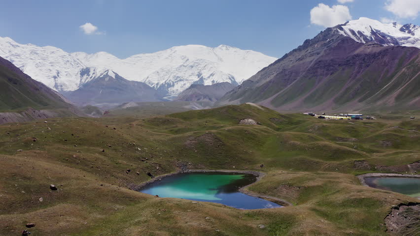 Panoramic flying drone movement over blue lakes at 3600m Base Camp, offering a vast panoramic view of the Pamir Mountains and lenin Peak wall.  Ibn Sina expedition in Kyrgyzstan, Central Asia.