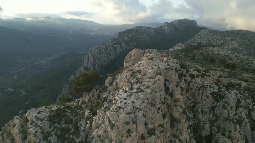 Majestic aerial view flying over a rugged mountain ridge surrounded by a vast green valley