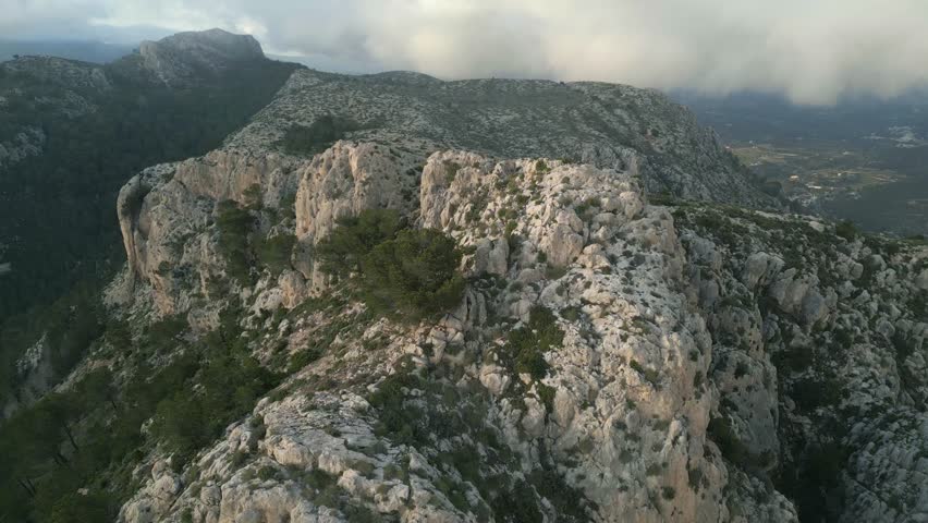 Majestic aerial view flying around a rocky mountain ridge covered with sparse vegetation at sunset