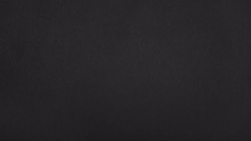 Diagonal-vertical rip splits real black paper; first the left part slides out, then the right paper follows.