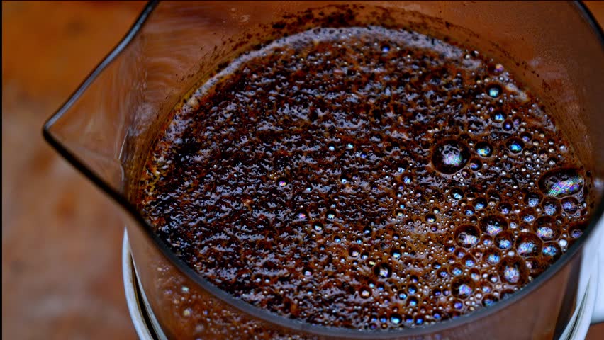 Zoom out revealing coffee bloom bubbles in French press. Macro view of crust and foam forming on top of hot coffee. Brewing process details and fresh aroma texture.