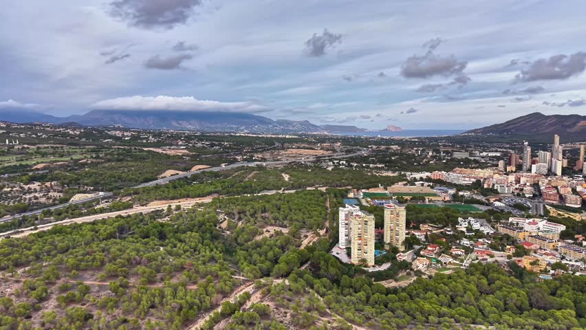 aerial view city skyline under clouds with lush forest foreground and distant river, urban planner surveying