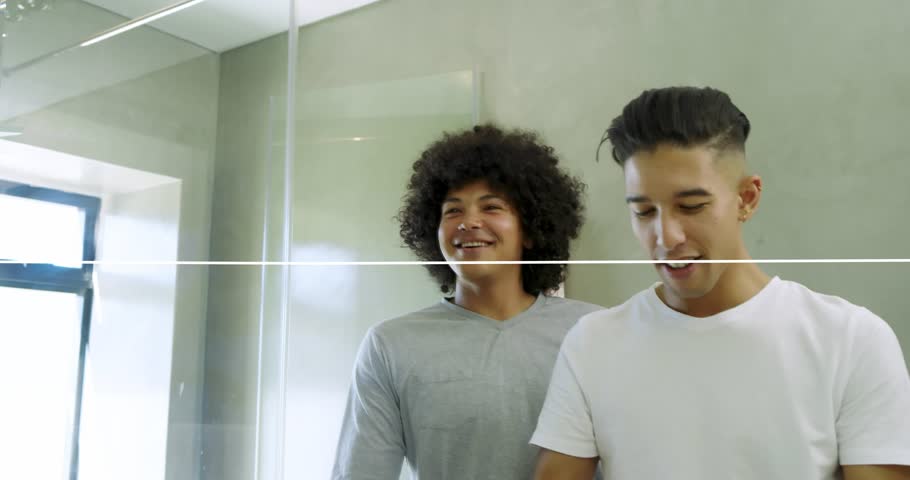 Two men grooming in bathroom, waveform sweeping across mirror initiating skincare and hair styling. Duo, friends, home, modern, reflection, facial, skin