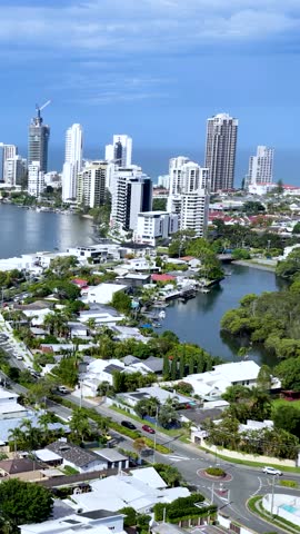 Drone pans over waterfront homes, canals, and high-rise skyline under bright daylight in Gold Coast