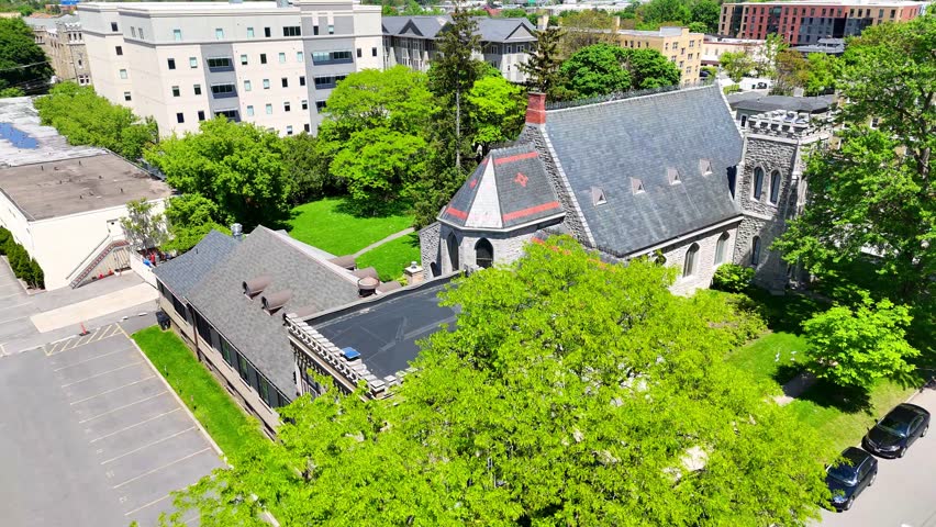 Aerially circling an Episcopalian church designed in the architectural style of gothic revival surrounded by the counterparts of a city.