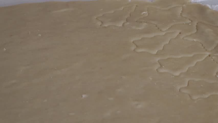 A close up of a Snowman shaped cookie cutter being used to make shaped Christmas cookies on a sheet of cookie dough.