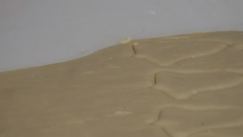 A close up of a star shaped cookie cutter being used to cut out a shaped cookie on a sheet of holiday cookie dough.