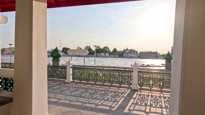 Slow pan across riverside promenade toward distant temple silhouette at warm sunset light