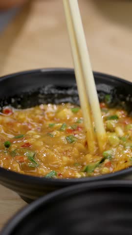Close-up of chopsticks stirring chunky spicy Asian chili garlic dipping sauce in black bowl