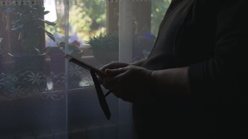 Closeup of an elderly woman standing by a window holding a photo frame, looking at it with emotion, reflecting memories and nostalgia in a quiet moment.