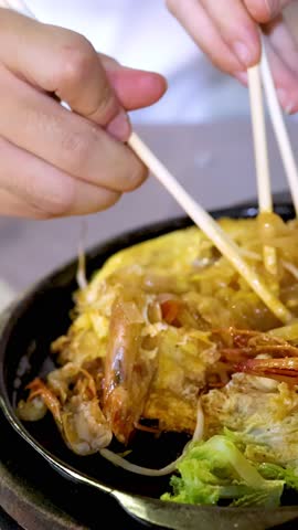 Close-up chopsticks lift steaming seafood pad thai noodles from sizzling hot plate in night market