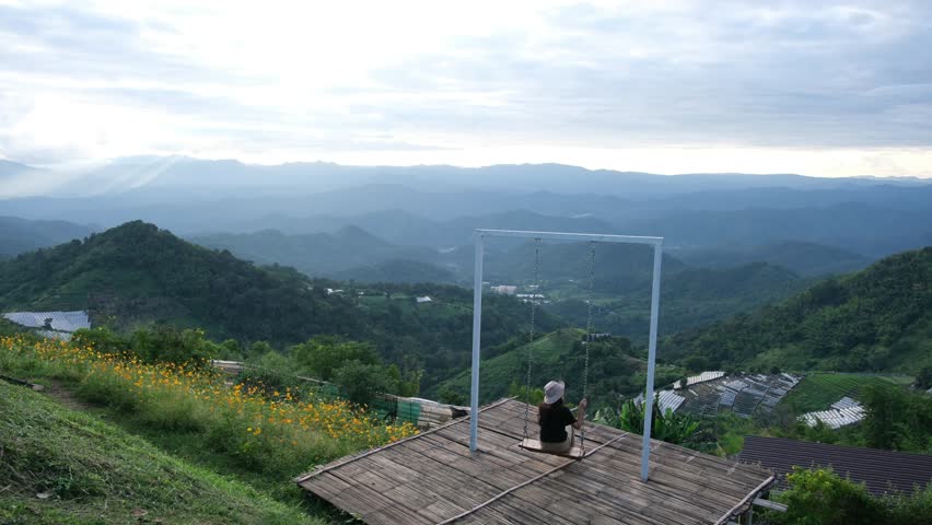 A woman sitting on a swing with a beautiful mountain views on cloudy day