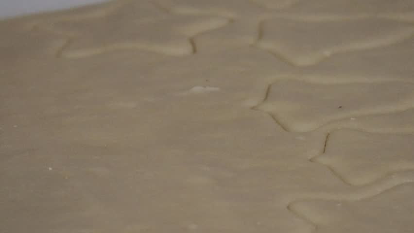 A star shaped cookie cutter being pressed into cookie dough, surrounded by various holiday shaped cookies.