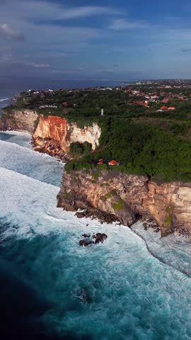 Aerial vertical view of Bali’s coastline featuring tall cliffs, breaking ocean waves, and golden light during sunset, revealing the raw tropical landscape and breathtaking coastal formations.
