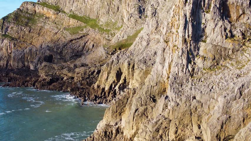 Low Orbiting Aerial of Eroding Rocky Coastline with Grassy Banks and Sheer Cliffs. Beautiful Welsh Gower Peninsula Coast. Travel Nature Drone Clip.