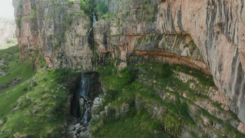 Drone pans across tall layered canyon waterfall with mossy rock walls in Kurdistan near Erbil.