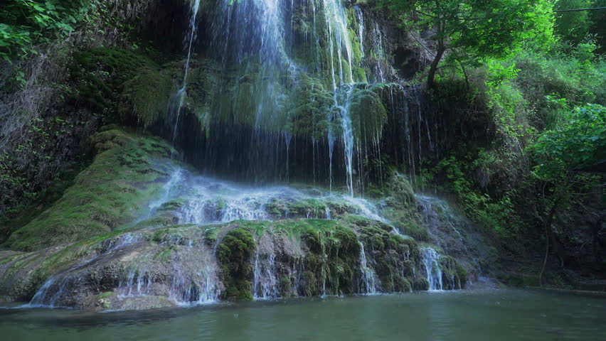 Low drone glides toward mossy Kurdish waterfall with fast flowing streams.