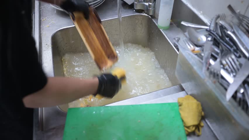 Restaurant worker washing dirty dishes in a kitchen sink