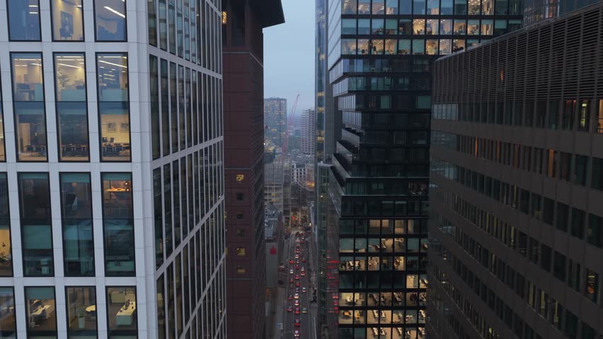 Aerial shot between modern skyscrapers in Frankfurt banking district at dusk. Street traffic below the offices while workers finish their day