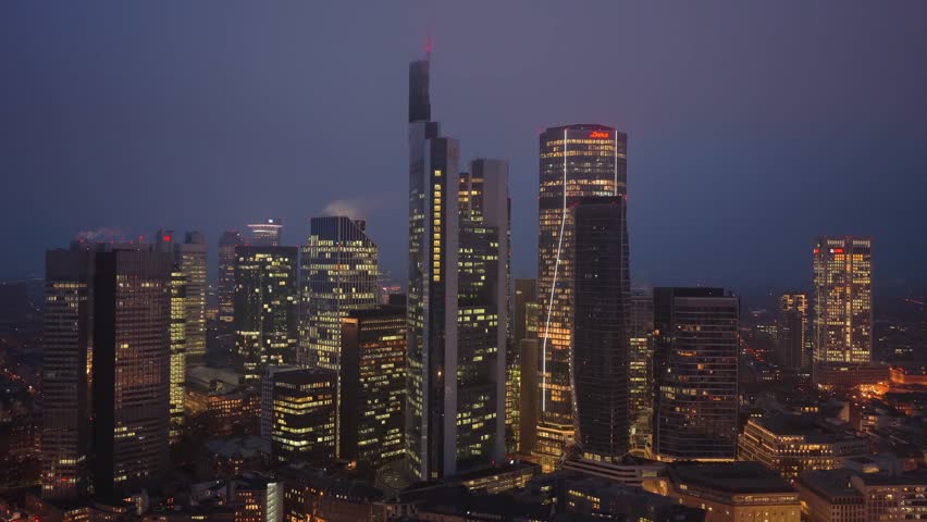Aerial footage of illuminated Frankfurt skyline at dusk. Modern skyscrapers and high rise office buildings like Commerzbank Tower light up the city