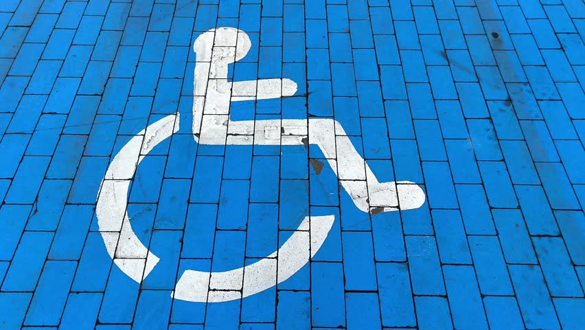 Close-up of a white wheelchair accessibility symbol painted on a vibrant blue tiled surface. This universal icon denotes a designated space for wheelchair users, promoting inclusivity in public areas.
