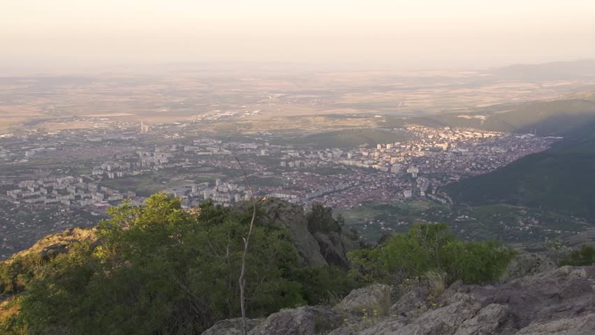 The camera shows Sliven city from a high point in the Balkan Mountains. The sun casts light on the buildings and landscape. Stara planina above Sliven town.