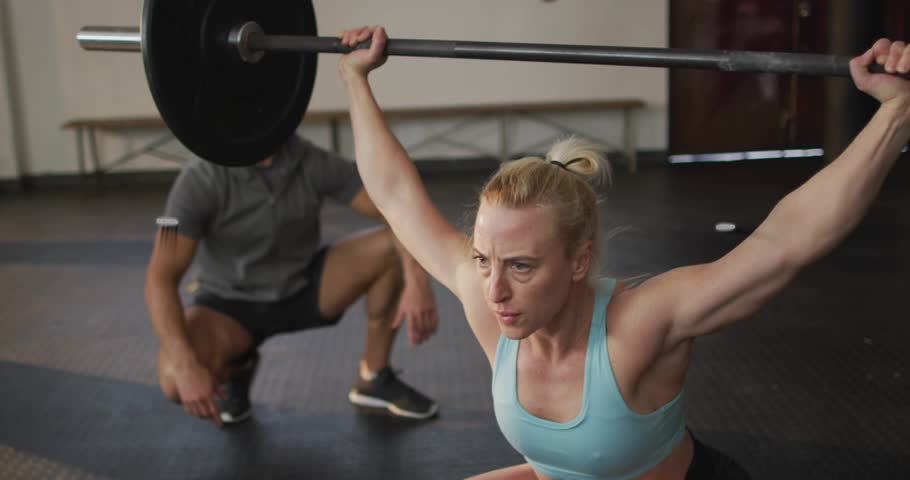 Woman lifter lowering bar into overhead squat AR tracking motion or force for training coach spotting. Weightlifting, gym, athletic, strength, focus, sunlit, analytics
