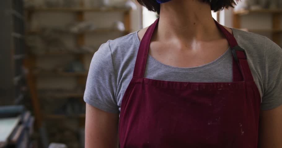 Ceramic maker turning as camera rising, revealing mask as virus icons filling, showing health risk. Pottery, studio, artisan, backlit, focused, overlays, graphics