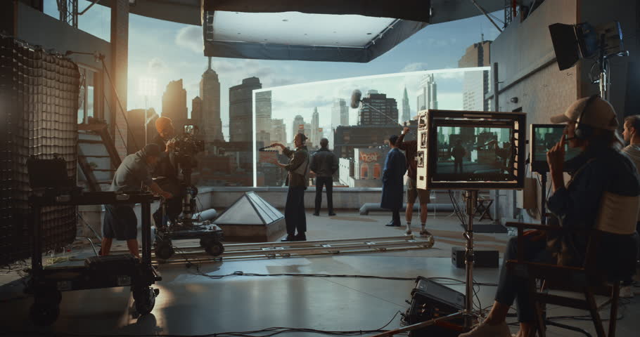 Behind-the-scenes of Dramatic Action Movie Filmed on a Rooftop Set, Crew Operate a Tracking Camera, Actors Performing Against Large Virtual Production Led Screen Displaying Futuristic City