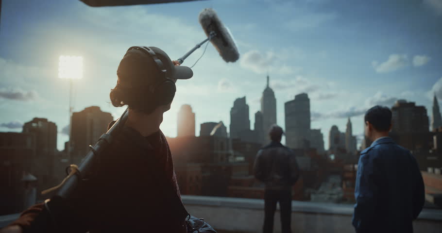 Professional Soundman Operates Boom Microphone While Two Actors Perform Dialogue on Movie Set Rooftop, Capturing Production Audio During Dramatic Film Scene in Studio Cinematic Storytelling