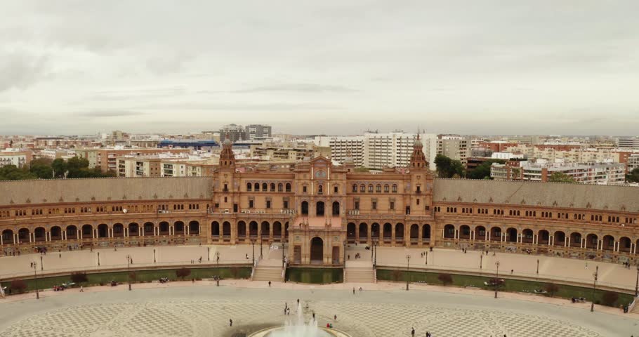 Expansive high-angle aerial view of the iconic Plaza de España in Seville, Spain, featuring the massive, symmetrical, semi-circular Renaissance Revival building, the central fountain and plaza