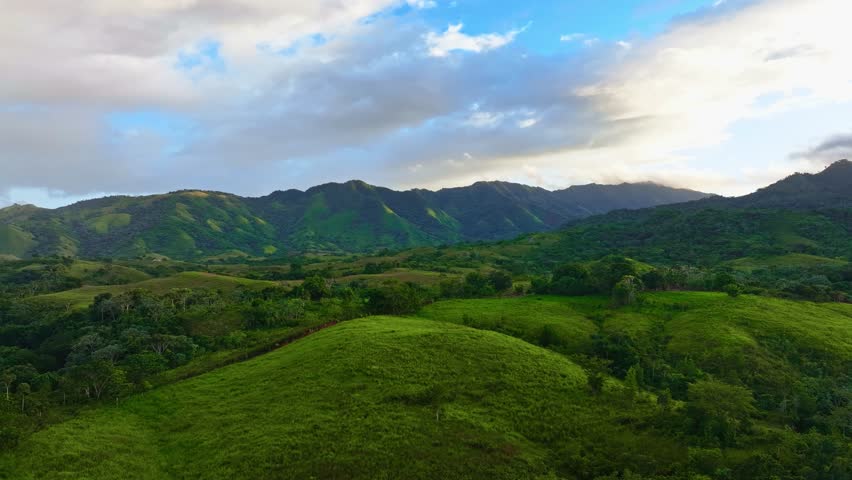 Amazing mountain landscape under a cloudy sky. A natural, open backdrop for travel. Beautiful scenery with forests, hills, and meadows in the evening light. A ridge with a high peak in the distance.