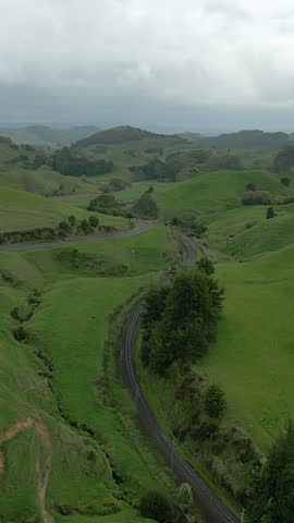 Flyover above railroad tracks, country road running through rolling hills, New Zealand, vertical orientation.