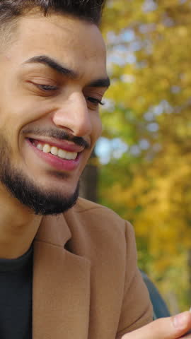Hispanic smiling happy man using mobile phone in autumn city park cheerful smile guy sitting on bench holding smartphone enjoying black friday online shopping purchase male outdoors browsing device