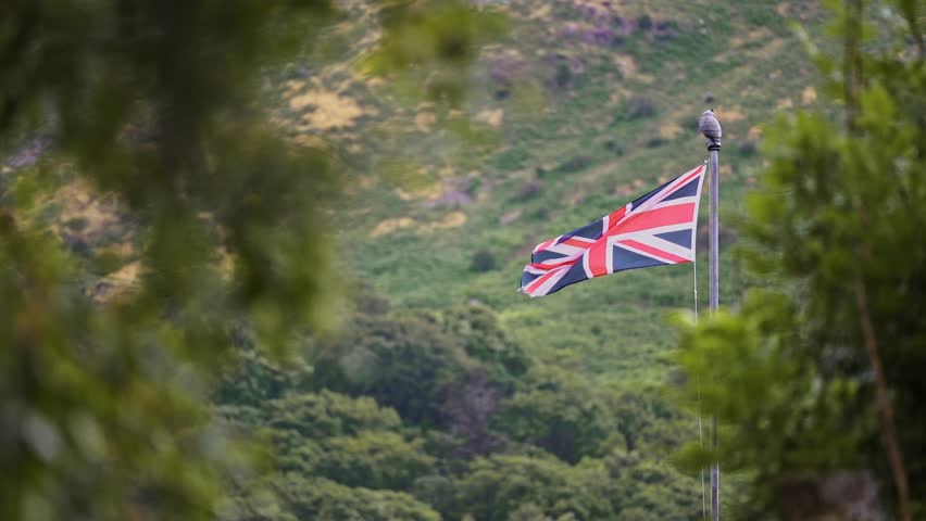 A Union flag flutters in the wind with a scenic mountain backdrop, capturing a patriotic and natural outdoor scene
