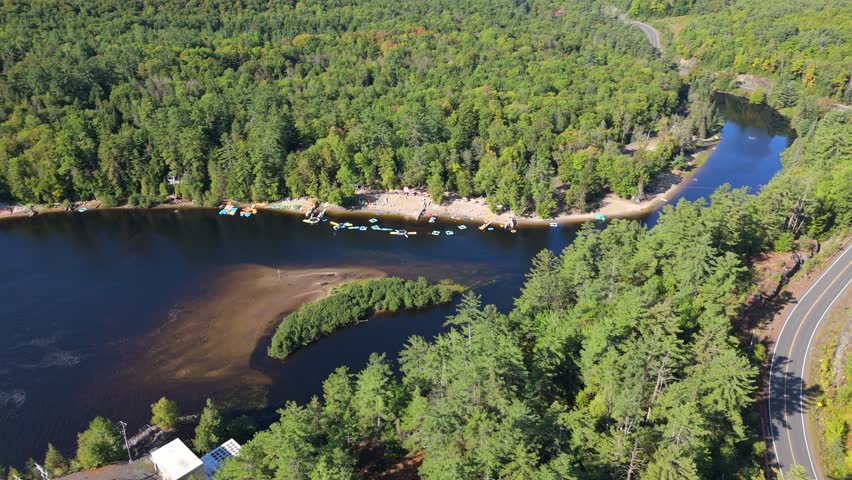 Aerial view of a sandy beach along the Muskoka River near High Falls, showing anchored kayaks and paddleboards set against dense forest and calm winding water.