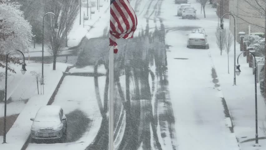 Aerial pedestal up shot of waving American flag on snowy winter in American city. Rising shot. Snow covered streets and houses in winter season. Patriotism town of USA.