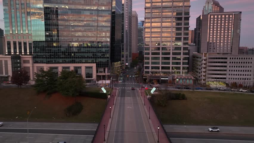 Sunset aerial of Charlotte, North Carolina, showing modern glass skyscrapers reflecting warm evening light, central avenue leading into uptown district. Aerial approaching shot. Traffic on interstate