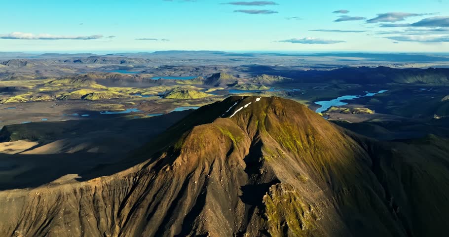A dramatic trailer-style aerial over Iceland’s volcanic peak, revealing ripped crater walls, vast glowing plains and distant lakes in a sweeping, high-energy cinematic reveal.